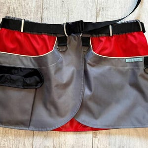 May include: A grey and red dog training belt with a black belt and multiple pockets. The belt has a label that says "Dogs & Walks".