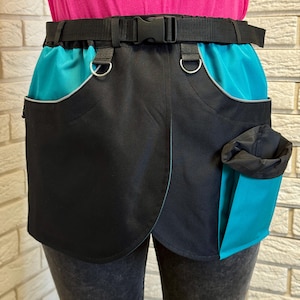 May include: Black and teal dog walking bag with a black adjustable belt and a plastic buckle. The bag has two teal pockets with silver trim and a teal bag dispenser.