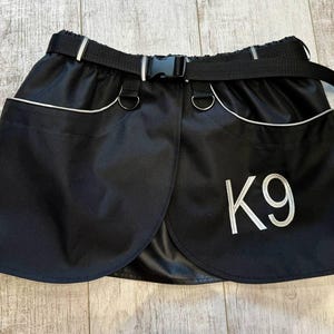 May include: Black dog training skirt with a white K9 logo and a black adjustable belt.