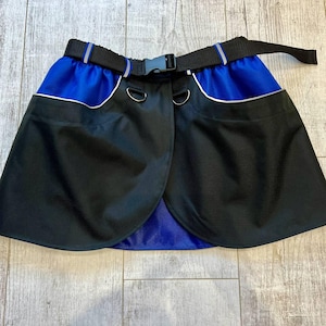 May include: Black and blue wrap skirt with a belt and two pockets. The skirt has a silver trim around the pockets and a silver stripe on the belt.