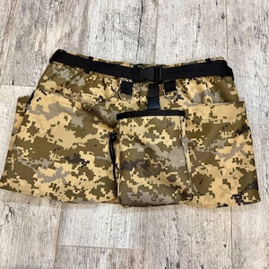 May include: A camouflage-patterned utility skirt with a black belt and a matching camouflage pouch. The skirt has multiple pockets and a drawstring closure.