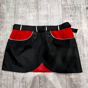 May include: A black skirt with red trim and two pockets. The skirt has a black belt with a silver buckle.