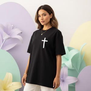 May include: Black t-shirt with a white cross graphic. The shirt is a classic crew neck style and appears to be made of a soft material. The cross is centered on the chest.