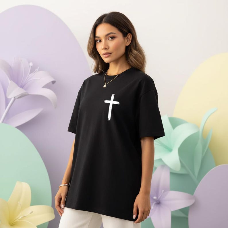 May include: Black t-shirt with a white cross graphic. The shirt is a classic crew neck style and appears to be made of a soft material. The cross is centered on the chest.