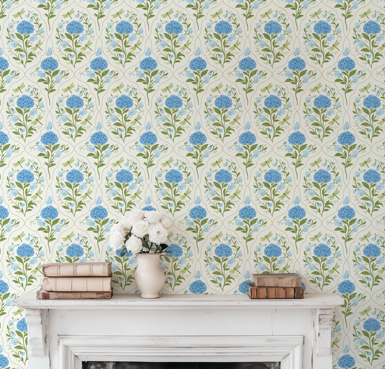 May include: Floral wallpaper featuring a repeating pattern of blue hydrangeas, green leaves, and dragonflies on a cream background. The image also shows a white mantel with books and a vase of white flowers.
