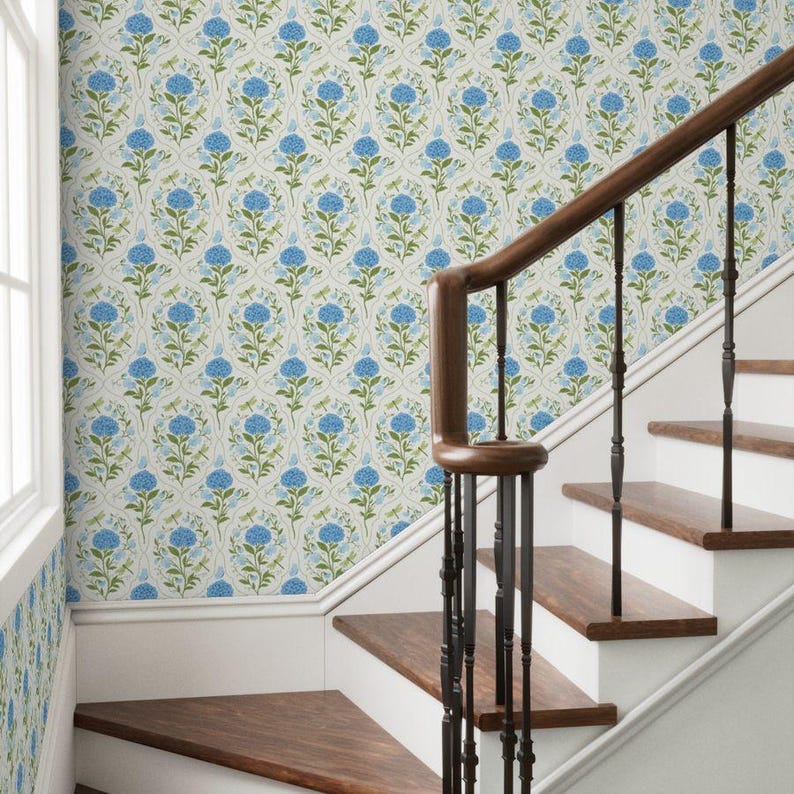 May include: A staircase with wooden steps and a dark brown handrail. The wall is covered in wallpaper with a repeating pattern of blue flowers and green leaves on a cream background. The stairs lead upwards.