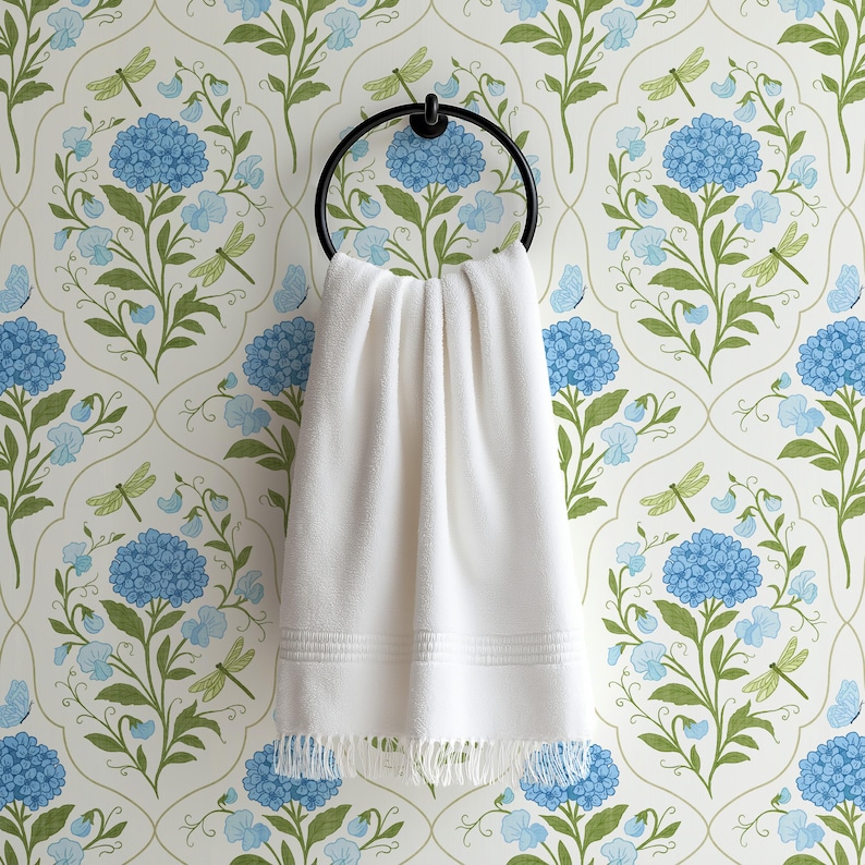 Close-up of a white hand towel hanging on an oil-rubbed brass ring, with blue hydrangea floral wallpaper in the background featuring butterflies and dragonflies on a white background.