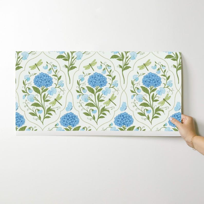 May include: A roll of wallpaper featuring a repeating pattern of blue hydrangea flowers, green leaves, and dragonflies on a cream background. The design includes light blue butterflies and a stylized floral motif.