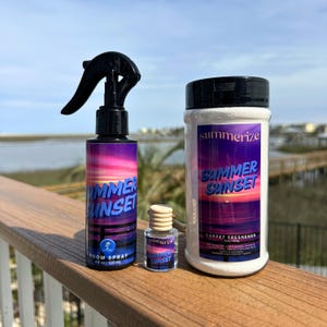 May include: A collection of Summer Sunset scented products, including a room spray, a small bottle, and a carpet freshener. The room spray is 4 fl oz (120 ml). Each product features a label with a sunset design in shades of purple, pink, and orange.