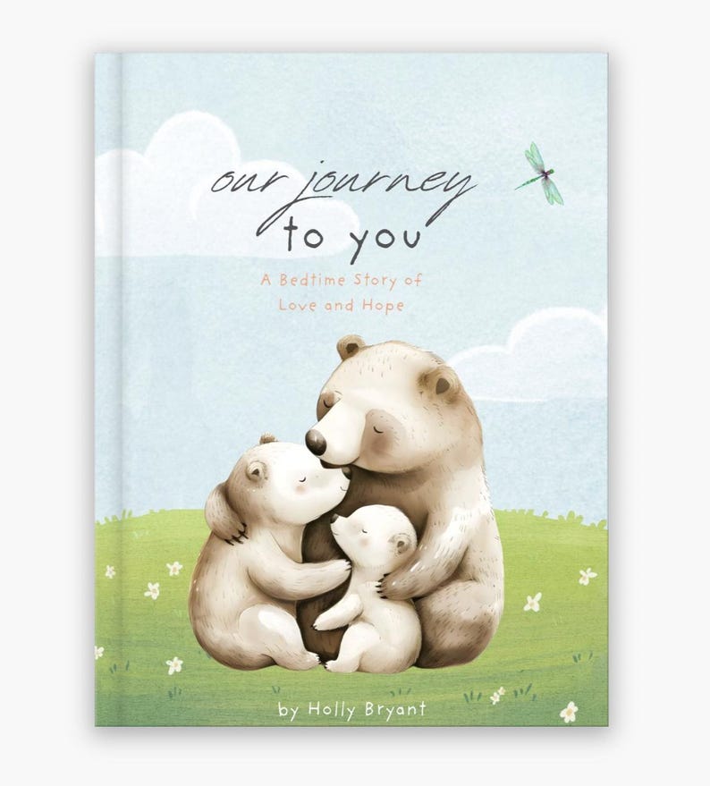 May include: A children's book cover with a blue background and white clouds. The title is "Our Journey to You" and the subtitle is "A Bedtime Story of Love and Hope". The cover features a family of bears hugging each other. The book is by Holly Bryant.