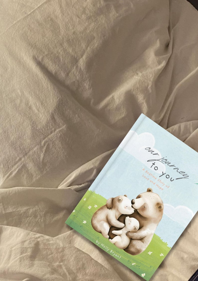 May include: A blue and white illustrated children's book titled "Our Journey to You: A Bedtime Story of Love and Hope" by Holly Bryant. The cover features a family of three bears hugging each other.