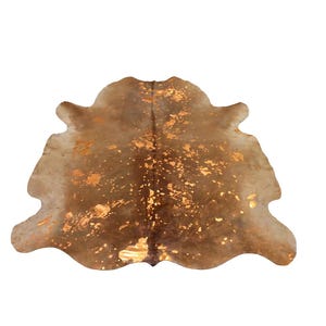 May include: A natural cowhide rug featuring a brown and tan base color with irregular metallic gold foil accents scattered across the surface. The hide has an organic, asymmetrical shape with a central seam and smooth, curved edges throughout.