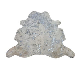 May include: A cowhide rug featuring an irregular, organic shape with a cream-coloured base and a metallic silver foil finish applied in a mottled, speckled pattern across the surface, creating a reflective and textured appearance throughout the piece.