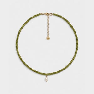Può includere: Una collana composta da piccole perline rotonde color verde oliva infilate insieme. Il pezzo include una chiusura a moschettone in metallo dorato, una catenella di estensione regolabile e un singolo piccolo ciondolo a goccia in perla bianca.