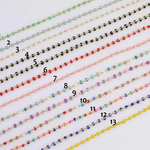 Peut inclure: Une collection de colliers de perles de différentes couleurs, dont le vert, le noir, le rouge, le rose, le violet et le jaune. Chaque collier est composé de petites perles colorées enfilées sur une chaîne dorée. Les colliers sont disposés en rangées parallèles.
