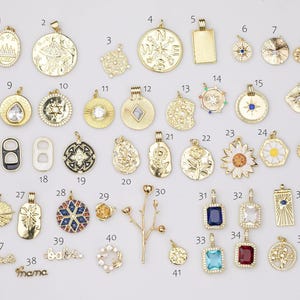 Op de afbeelding: Een verzameling goudkleurige hangers en bedels in verschillende vormen en ontwerpen. Inclusief een kompas, een rechthoek, een madeliefje, een ster en een bedel met het woord "mama".