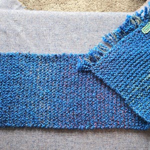 May include: A blue and pink woven scarf with a fringe on one end. The scarf is made of a soft, textured material.