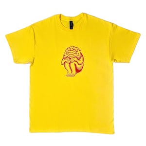 May include: A yellow t-shirt featuring a red illustration of a creature. The graphic is centered on the front of the shirt. The shirt has short sleeves and a crew neck.