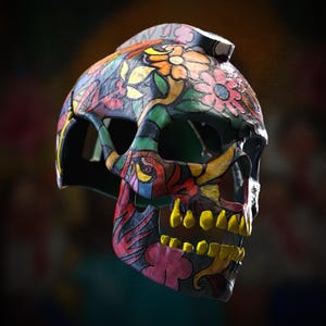 Puede incluir: Una calavera decorativa con un diseño floral colorido. La calavera presenta una base negra con vibrantes acentos de rojo, amarillo, verde y rosa. Los dientes están pintados de amarillo, y el diseño general es intrincado y detallado.