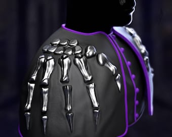 May include: A black shoulder cape with a skeleton hand design. The cape features silver bone accents and a purple trim. The design is set against a dark background, creating a gothic or fantasy aesthetic.