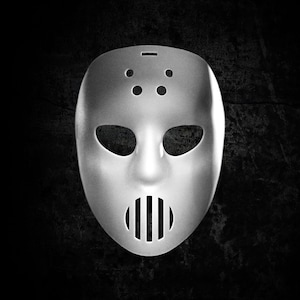 Pode incluir: Uma máscara de goleiro de hóquei de plástico branco com uma gaiola de metal preto sobre a boca.