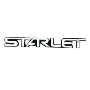 May include: A silver and black car emblem with the word "STARLET" in raised lettering.