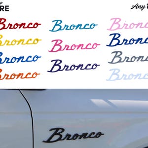 May include: A selection of Bronco decals in diverse colours, such as red, blue, yellow, and pink, featuring the word "Bronco" in a cursive script. The image also displays a black Bronco emblem on a white vehicle.