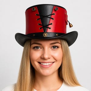 Puede incluir: Un sombrero de copa con diseño en negro y rojo y una corona estructurada. La parte frontal muestra un panel triangular negro con cordones negros entrelazados a través de ojales metálicos. Incluye tachuelas color latón y una pequeña campana.