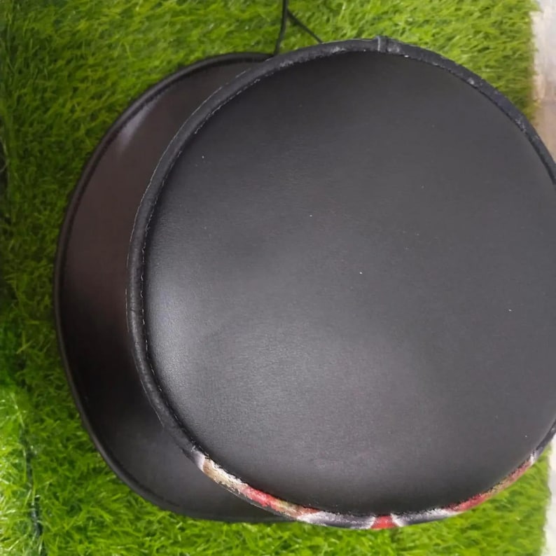 Puede incluir: Dos alas de sombrero negras y redondas, hechas de un material similar al cuero. Las alas est&aacute;n apiladas, con un borde estampado visible en la ala inferior. Las alas est&aacute;n sobre un fondo verde.
