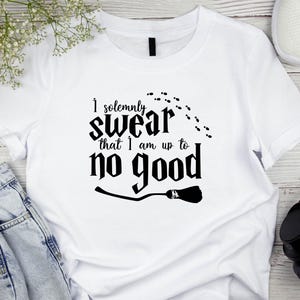 May include: White t-shirt with the phrase "I solemnly swear that I am up to no good" in black lettering. The design includes a broom and footprints. Casual wear.