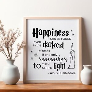 May include: A framed print featuring the quote "Happiness can be found even in the darkest of times if one only remembers to turn on the light - Albus Dumbledore." The print has a light wood frame, white background, and black text. A candle illustration is included.