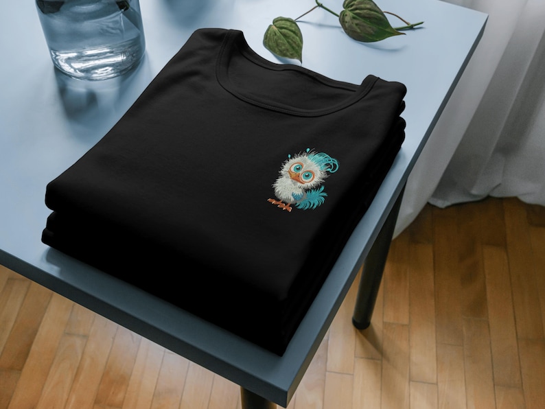 以下が含まれることがあります： 前面に青と白の漫画の鳥が刺繍された黒いTシャツ