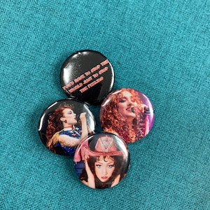 May include: Four round black button badges featuring images of a woman with long curly hair wearing a microphone, a woman with short hair wearing a microphone, a woman with long hair wearing a cowboy hat and a badge with the text "You've have to stop the world just to stop the feeling."