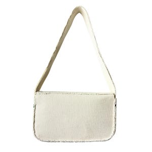May include: Off-white rectangular handbag with a matching shoulder strap. The bag has a textured surface and is trimmed with a silver-colored material. The strap is attached to the top of the bag and is made of a smooth, solid material.