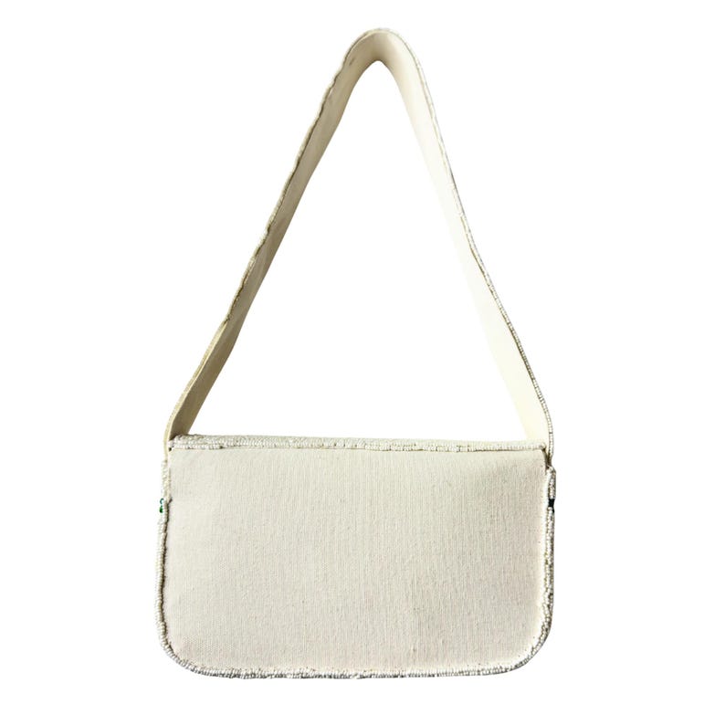 May include: Off-white rectangular handbag with a matching shoulder strap. The bag has a textured surface and is trimmed with a silver-colored material. The strap is attached to the top of the bag and is made of a smooth, solid material.
