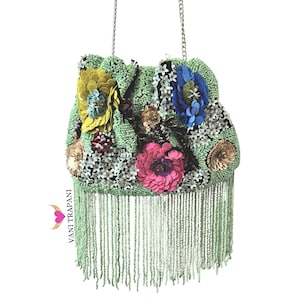 May include: A beaded handbag with a chain strap, featuring a light green base adorned with colorful floral embellishments. The flowers include yellow, blue, and pink petals, with a fringe of beads at the bottom. The bag is a unique accessory.