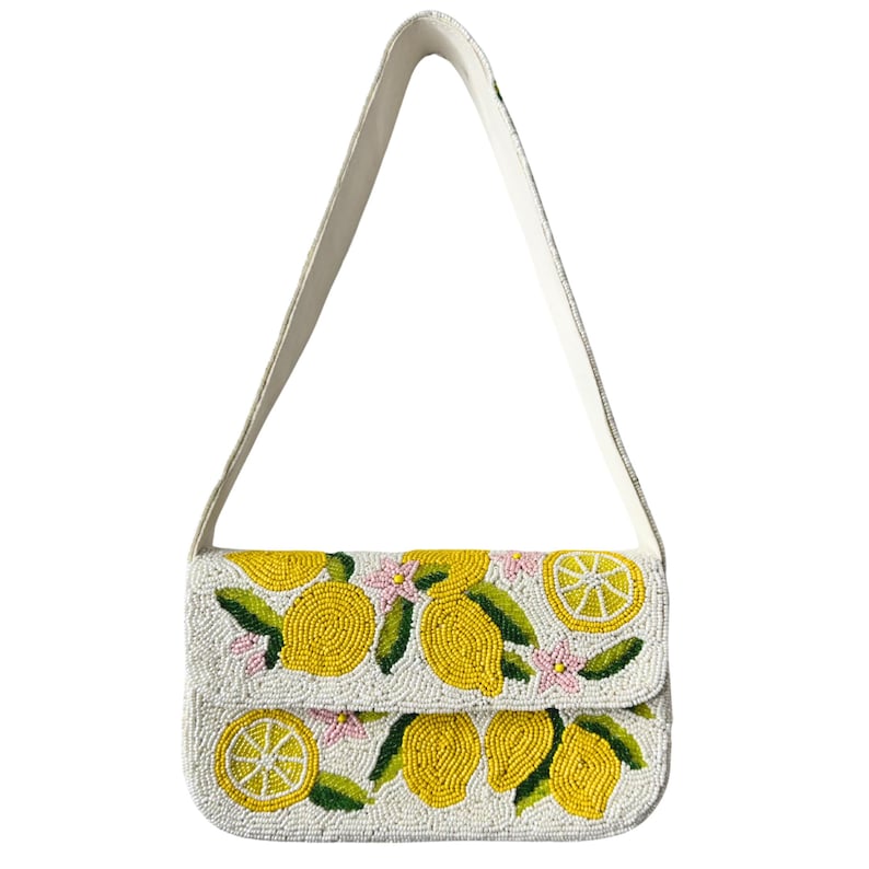 May include: A white beaded shoulder bag with a flap closure, featuring a lemon design. The bag has a white strap and is adorned with yellow lemons, green leaves, and pink flowers. The bag's dimensions are approximately 10 inches wide and 6 inches high.