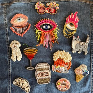 May include: A selection of beaded patches, featuring a dog, cat, cocktail, coffee cup, croissant, and ice cream cone. Other patches include eyes, a bicycle, a beer mug with fish, and a donut. The patches are in various colours.