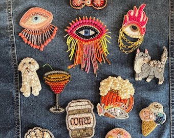 Puede incluir: Colección de parches bordados, que incluyen un perro, un gato, un cóctel, una taza de café, un cruasán y un helado. Otros parches incluyen ojos, una bicicleta, una jarra de cerveza con pescado y un donut. Los parches son multicolores.