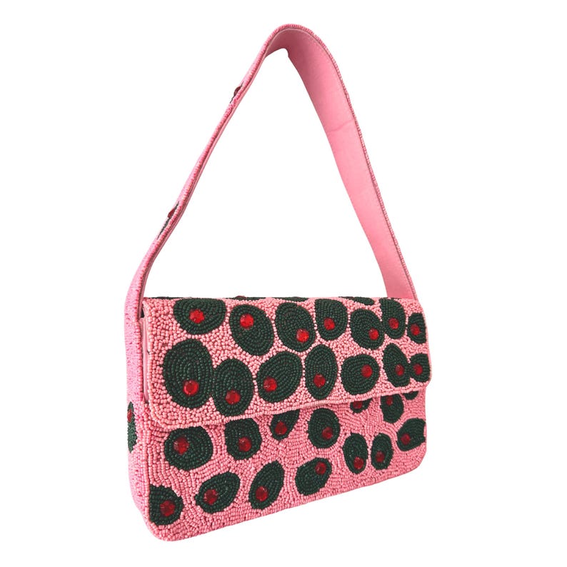 May include: Pink beaded shoulder bag with a flap closure. The bag features a pattern of dark green circles with red accents. The strap and the body of the bag are pink.