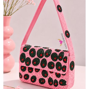 May include: Pink beaded handbag with a flap closure, featuring a pattern of green circles with red accents. The bag has a matching pink strap and the text "VANI TRAPANI".