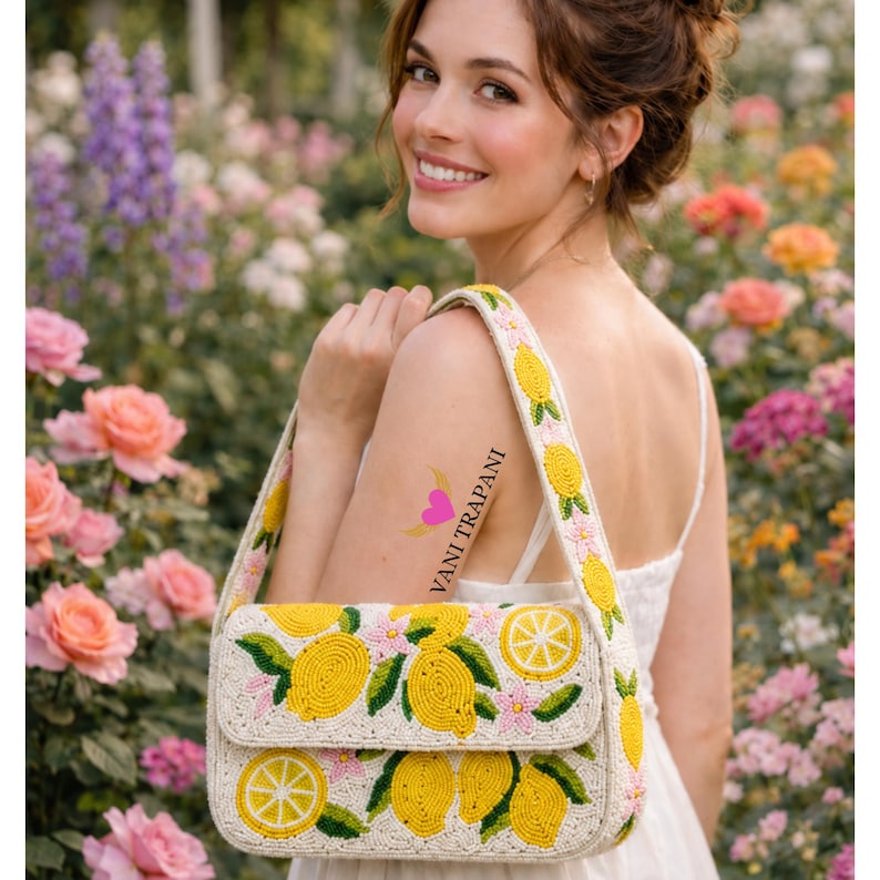 May include: A cream-colored handbag with a lemon design. The bag features yellow lemons and pink flowers, with a matching strap. The text "VANI TRAPANI" is visible on the woman's arm.