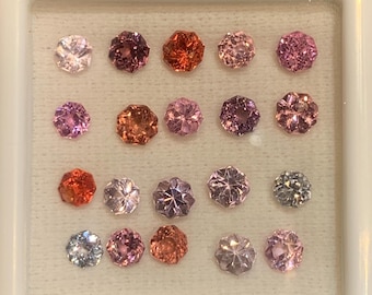 May include: A collection of 16 faceted gemstones in various shades of pink, red, and purple, displayed in a white tray.