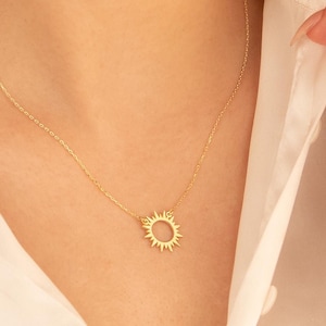 Könnte beinhalten: Eine goldene Halskette mit einem zarten Sonnenanhänger. Die Sonne ist ein einfacher Kreis mit nach außen gerichteten Strahlen.
