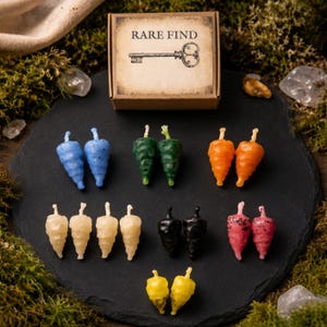 May include: A collection of small, cone-shaped candles in blue, green, orange, white, black, pink, and yellow, arranged on a dark circular surface. Above them sits a rectangular cardboard box labeled RARE FIND with a vintage key illustration.