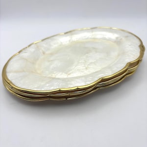 May include: A stack of three oval-shaped dishes featuring a pearlescent white, marbled surface with a smooth, glossy finish. Each dish is framed by a thin, metallic gold-toned scalloped edge that follows the curved perimeter of the plate.