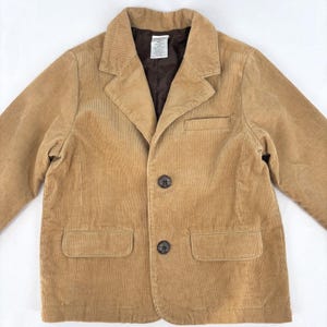 May include: A tan corduroy blazer with two front pockets and two buttons. The blazer has a notched lapel and a dark brown interior lining. The jacket is a classic style.