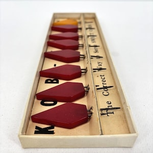 May include: A vintage set of red and orange Bakelite buttons in a rectangular box. The buttons are diamond-shaped with metal pins. The box has text that reads "The Correct Way".
