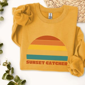 May include: A mustard yellow sweatshirt with a retro sunset graphic and the text "SUNSET CATCHER".