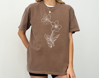 May include: A brown oversized t-shirt with a white outline of a flower design. The shirt has a relaxed fit and a crew neck.